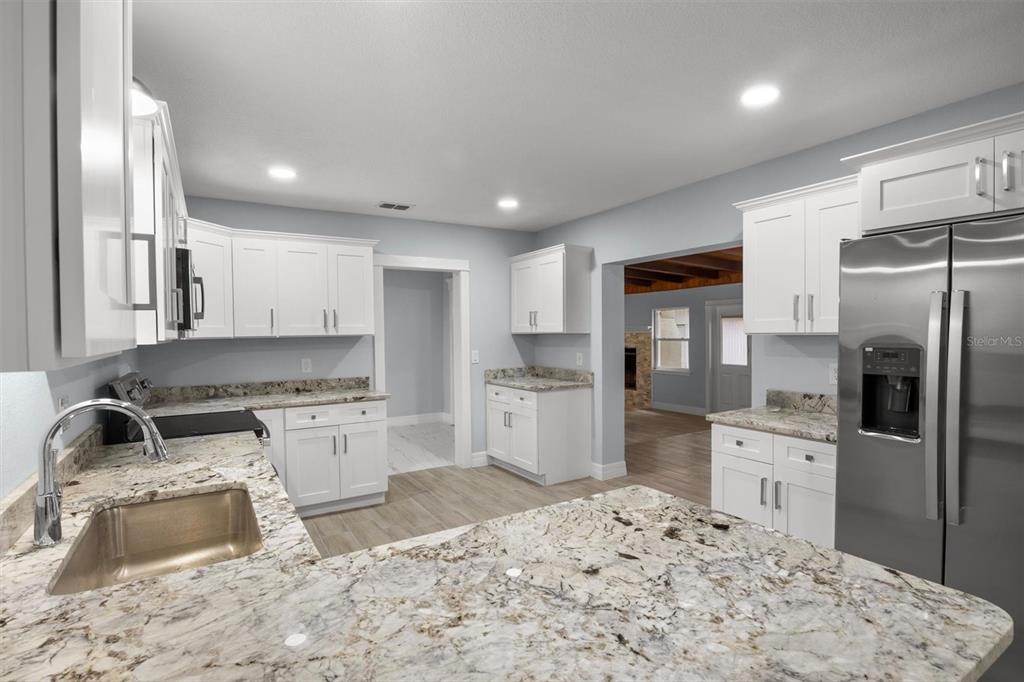 A kitchen with white cabinets, granite countertops, stainless steel appliances, and light wood-look flooring — 3945 CHART PRINE ROAD, LAKELAND, FL