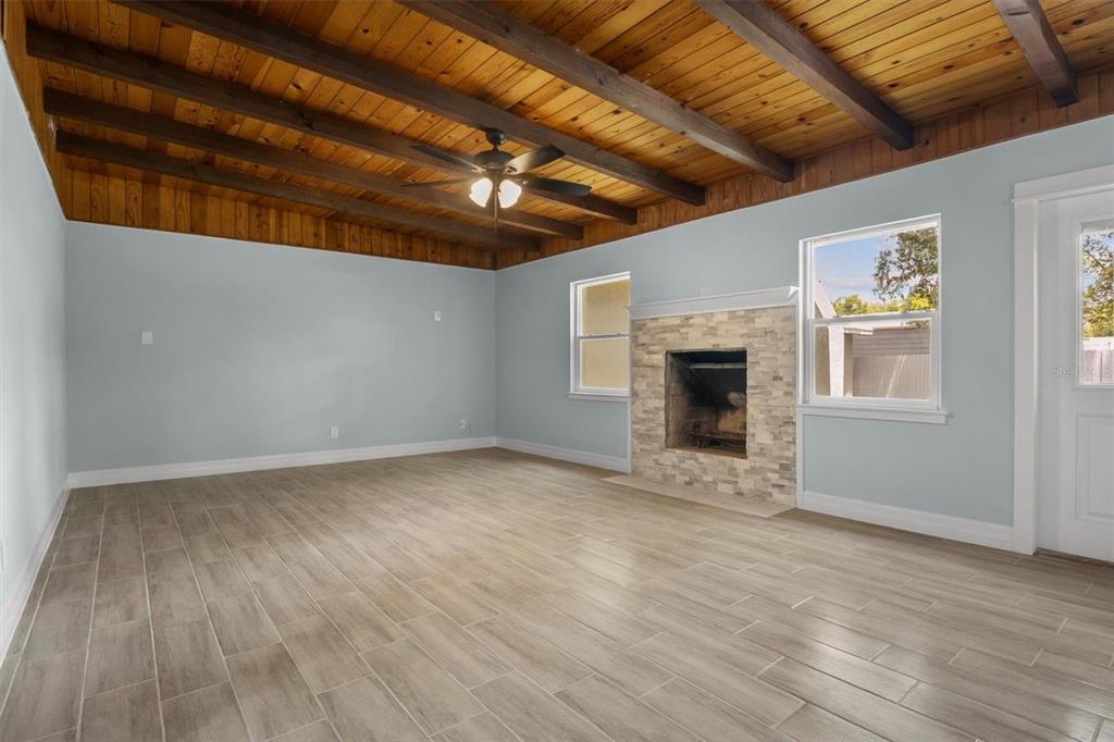 A living room features a wood-beamed ceiling, light blue walls, tile flooring, and a stone fireplace — 3945 CHART PRINE ROAD, LAKELAND, FL