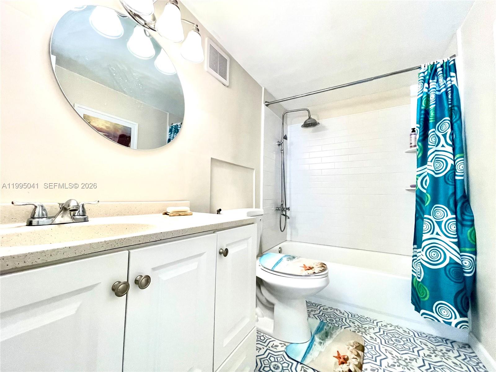 A bathroom features a white vanity, a round mirror, a toilet, and a tiled shower — 1913 S OCEAN DR # 129, Hallandale Beach FL 33009, HALLANDALE BEACH, FL