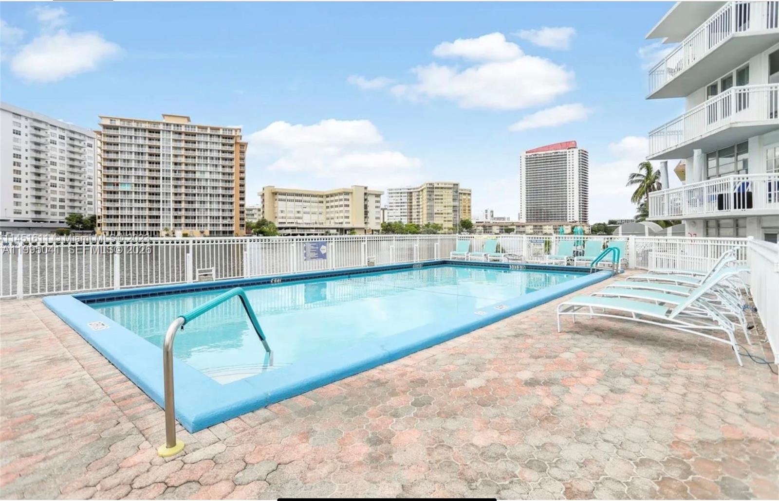 An outdoor swimming pool with lounge chairs on a paved deck surrounded by apartment buildings — 1913 S OCEAN DR # 129, Hallandale Beach FL 33009, HALLANDALE BEACH, FL
