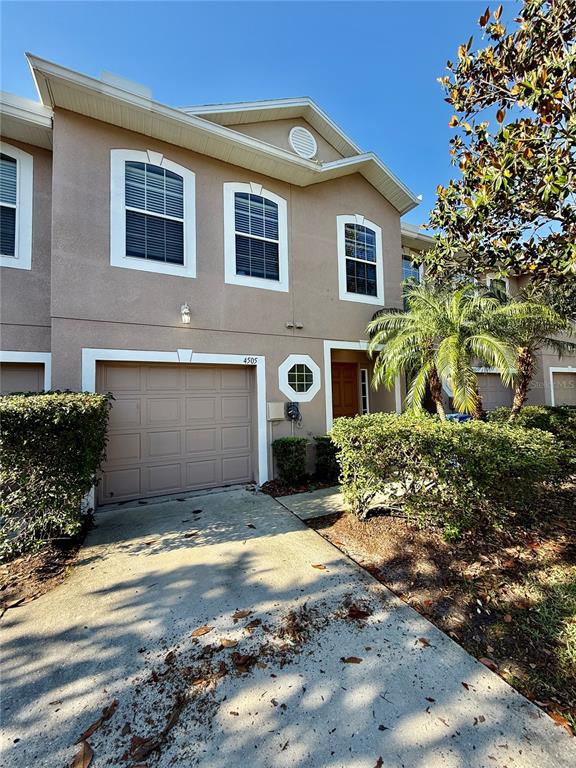 A two-story tan townhouse features a single-car garage and a concrete driveway — 4505 ASHBURN SQUARE DRIVE, TAMPA, FL