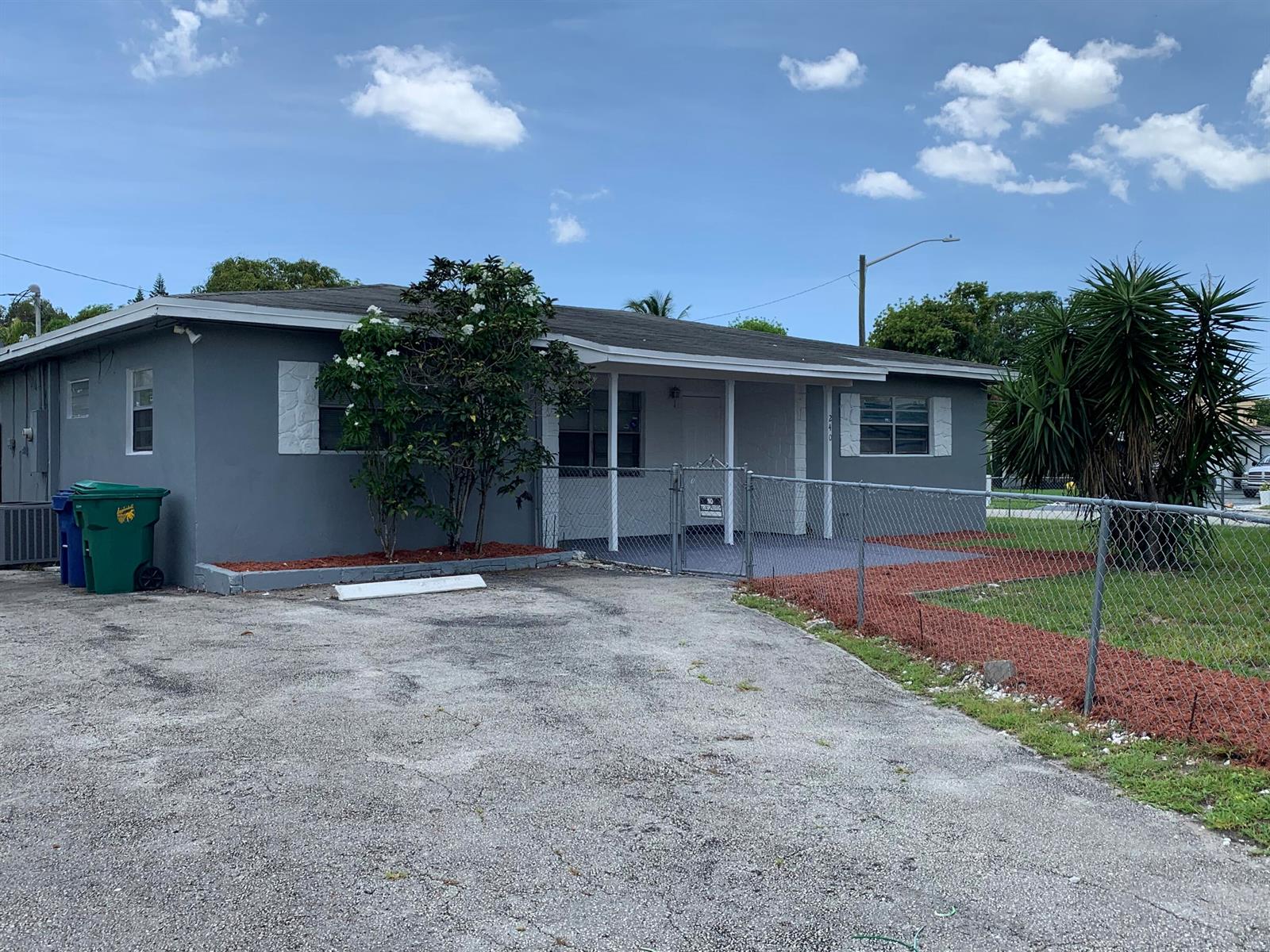 A gray single-story house features a front porch, a chain-link fence, and a paved driveway — 240 NW 38th Avenue, Lauderhill FL 33311, LAUDERHILL, FL