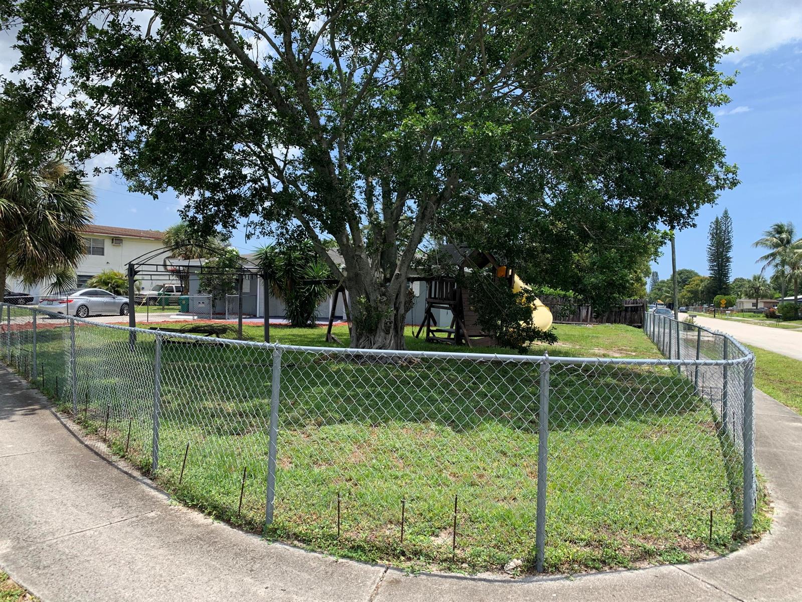 A fenced grassy yard features a large tree and a wooden playset — 240 NW 38th Avenue, Lauderhill FL 33311, LAUDERHILL, FL