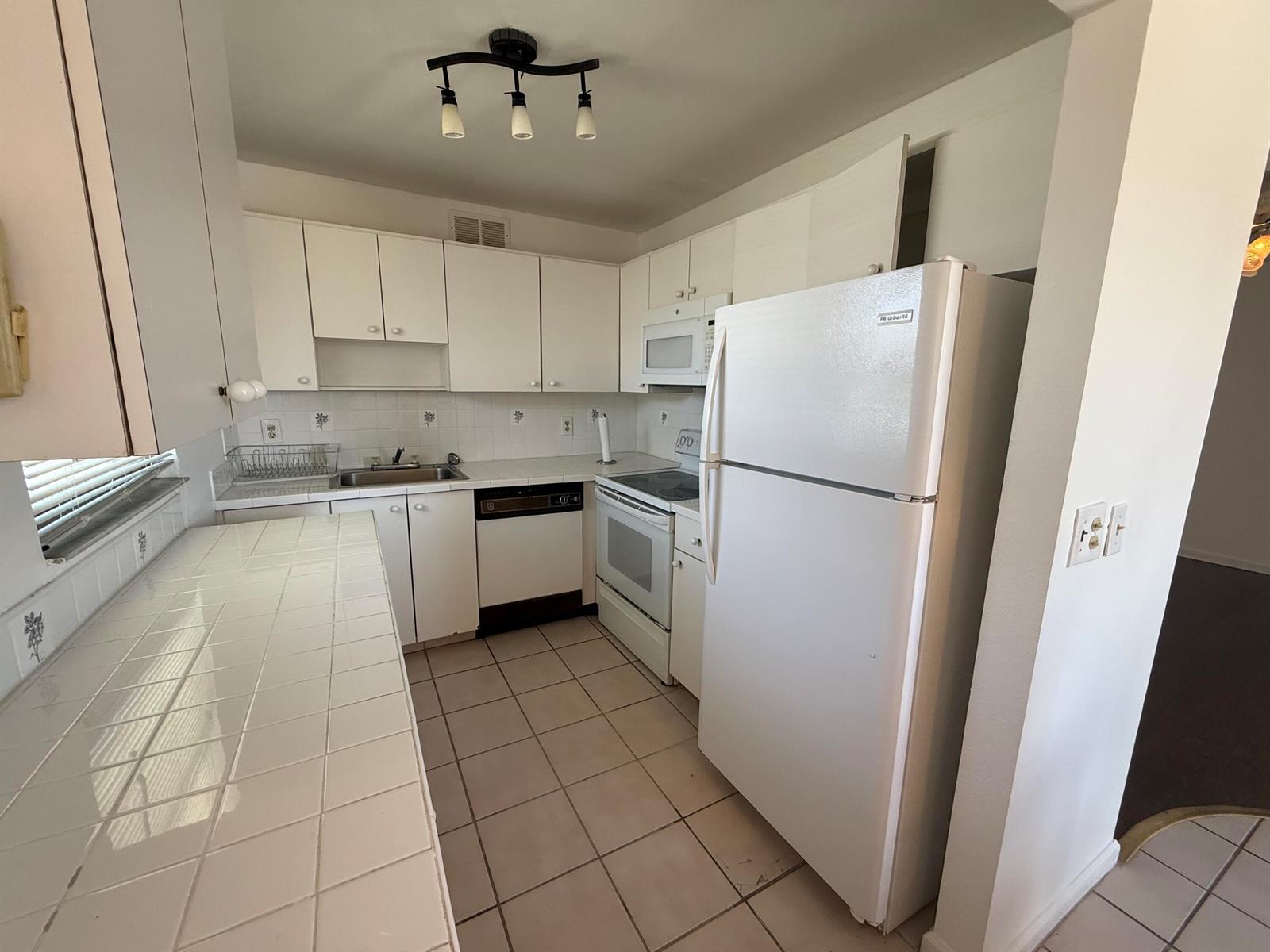 A kitchen features white cabinets, tiled countertops, a white refrigerator, and a tiled floor — 516 Saxony K, Delray Beach FL 33446, DELRAY BEACH, FL