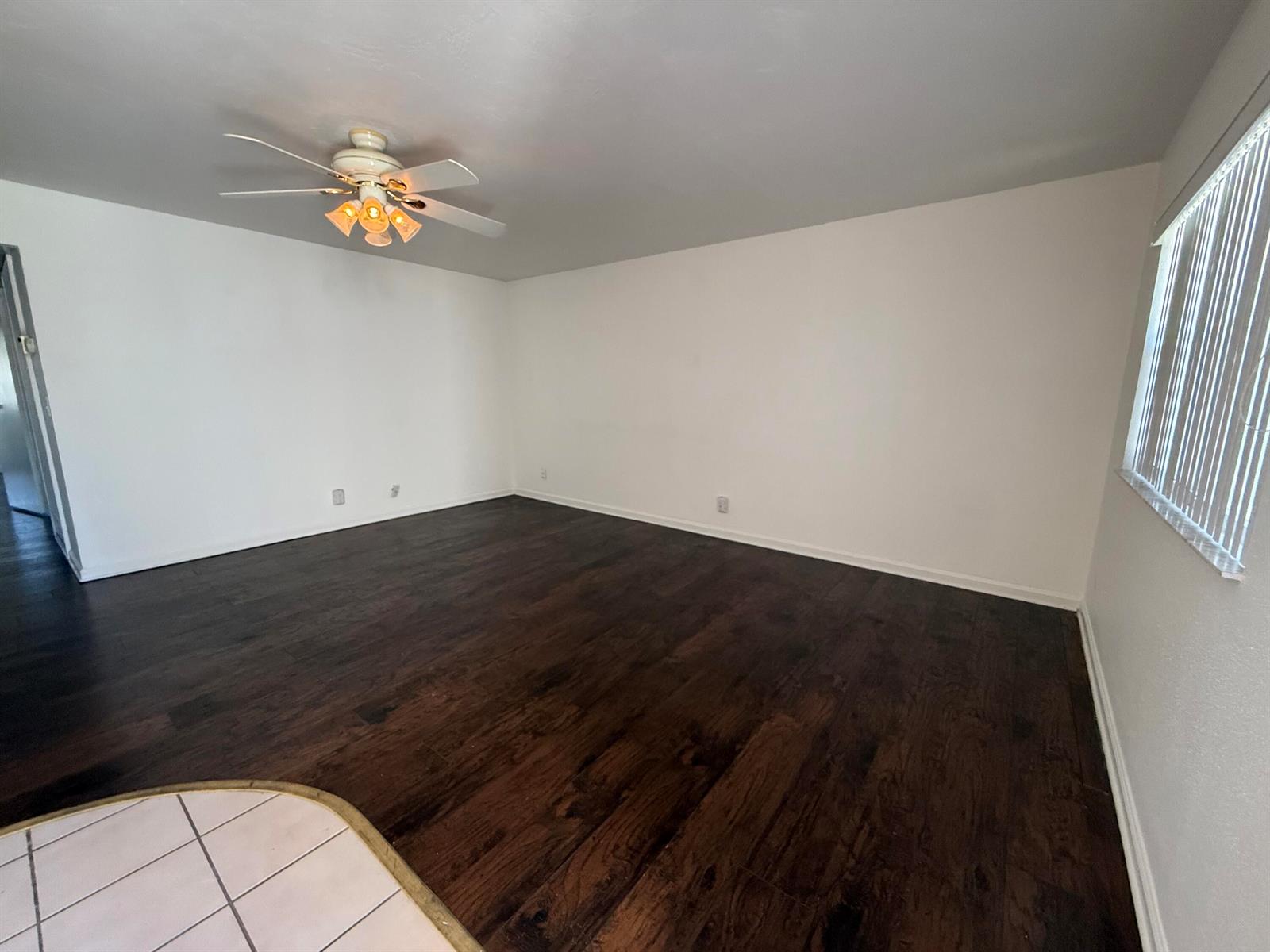 An empty room features dark wood flooring, white walls, and a ceiling fan with lights — 516 Saxony K, Delray Beach FL 33446, DELRAY BEACH, FL