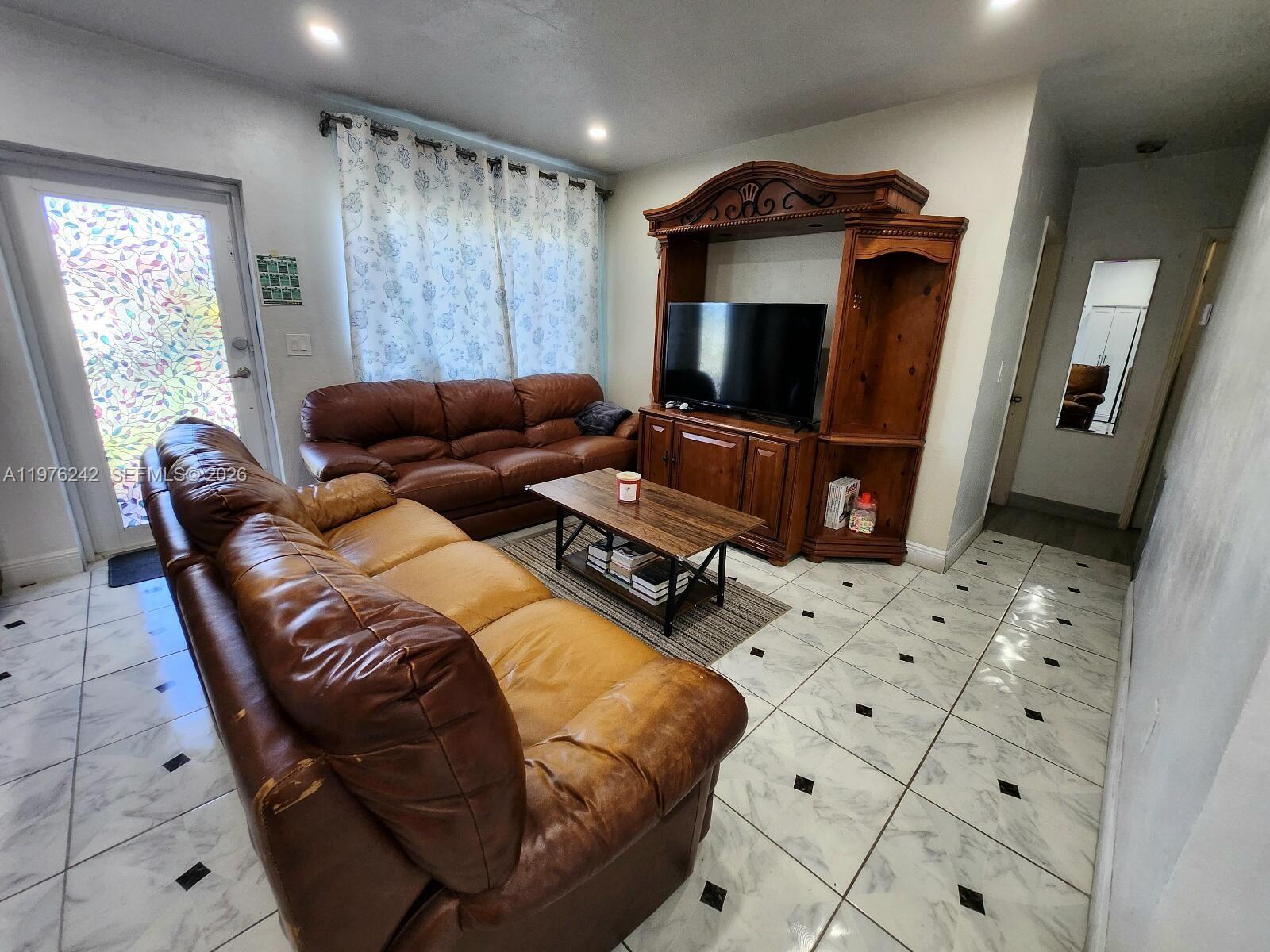 A living room features two brown leather sofas, a wooden entertainment center, and tiled floors — 3560 NW 19th St, Miami FL 33125, MIAMI, FL