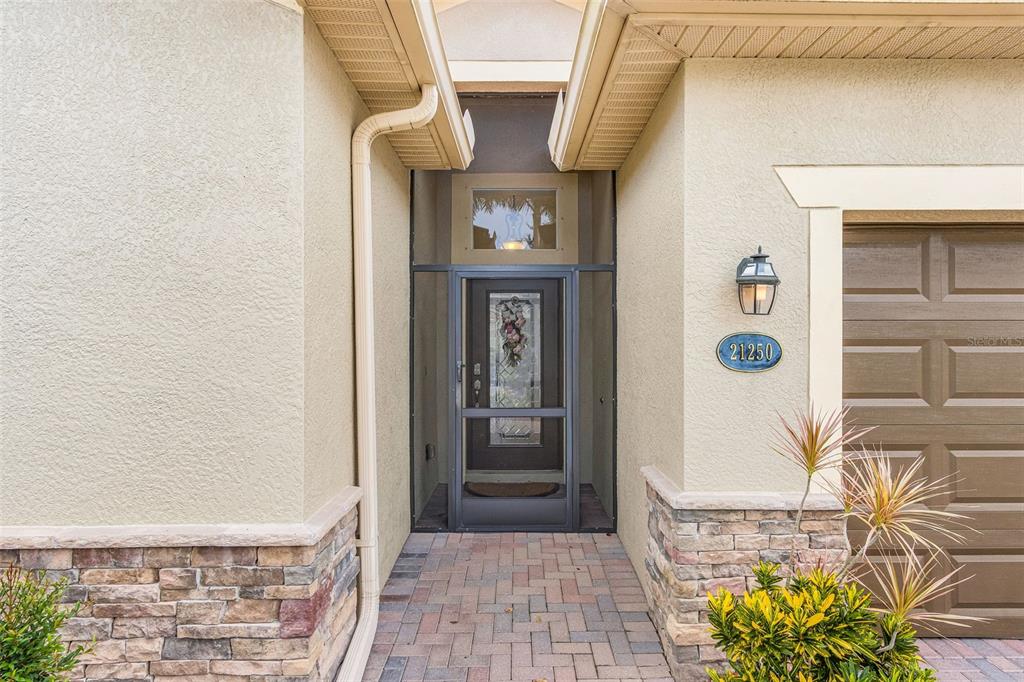 The exterior of a home features a stone-accented entryway with a screen door — 21250 BELLA TERRA BOULEVARD, ESTERO, FL