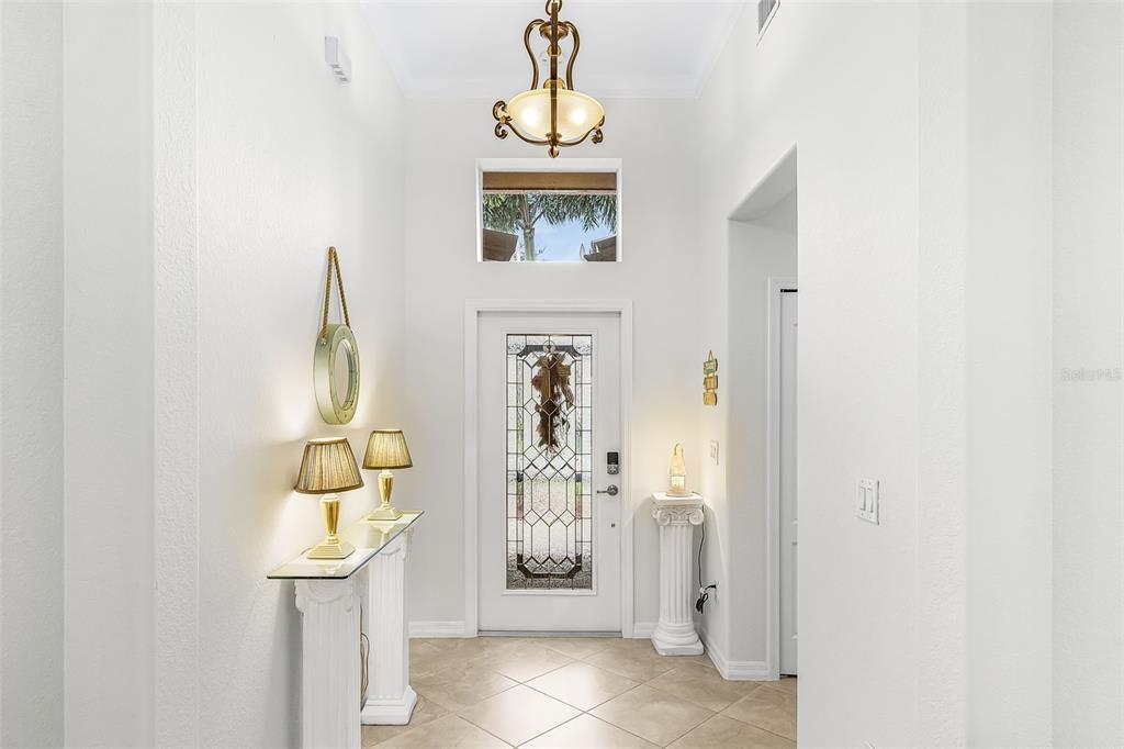 A bright entryway features a glass-paneled front door, a chandelier, and white pedestal tables — 21250 BELLA TERRA BOULEVARD, ESTERO, FL