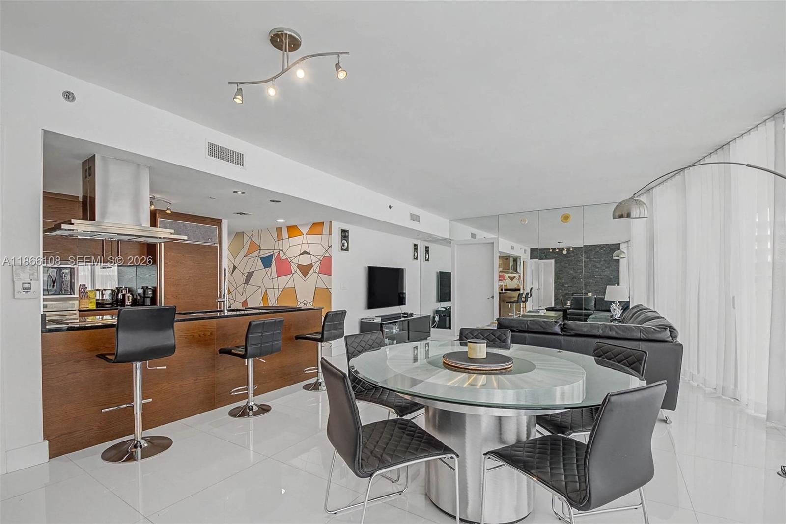 An open-concept living and dining area features a modern kitchen, glass table, and mirrored walls — 495 Brickell Ave # 3504, Miami FL 33131, MIAMI, FL