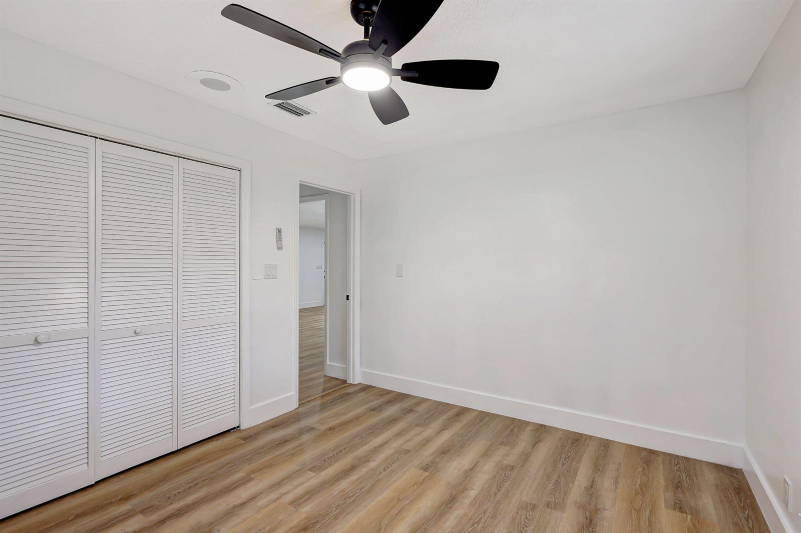 An empty bedroom features white walls, wood-look flooring, a ceiling fan, and white louvered closet doors — 1825 39th Avenue, Vero Beach FL 32960, VERO BEACH, FL