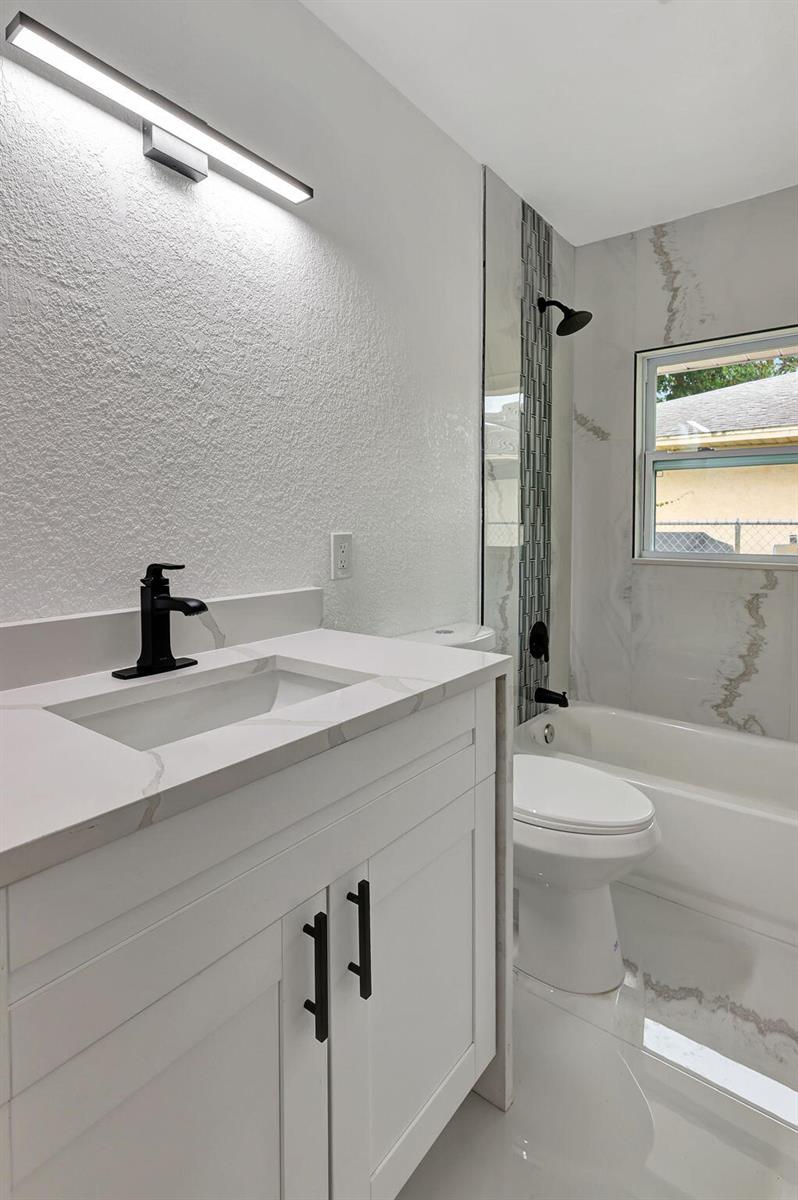 A modern bathroom features a white vanity, marble-look countertop, black fixtures, and a tiled tub — 1825 39th Avenue, Vero Beach FL 32960, VERO BEACH, FL