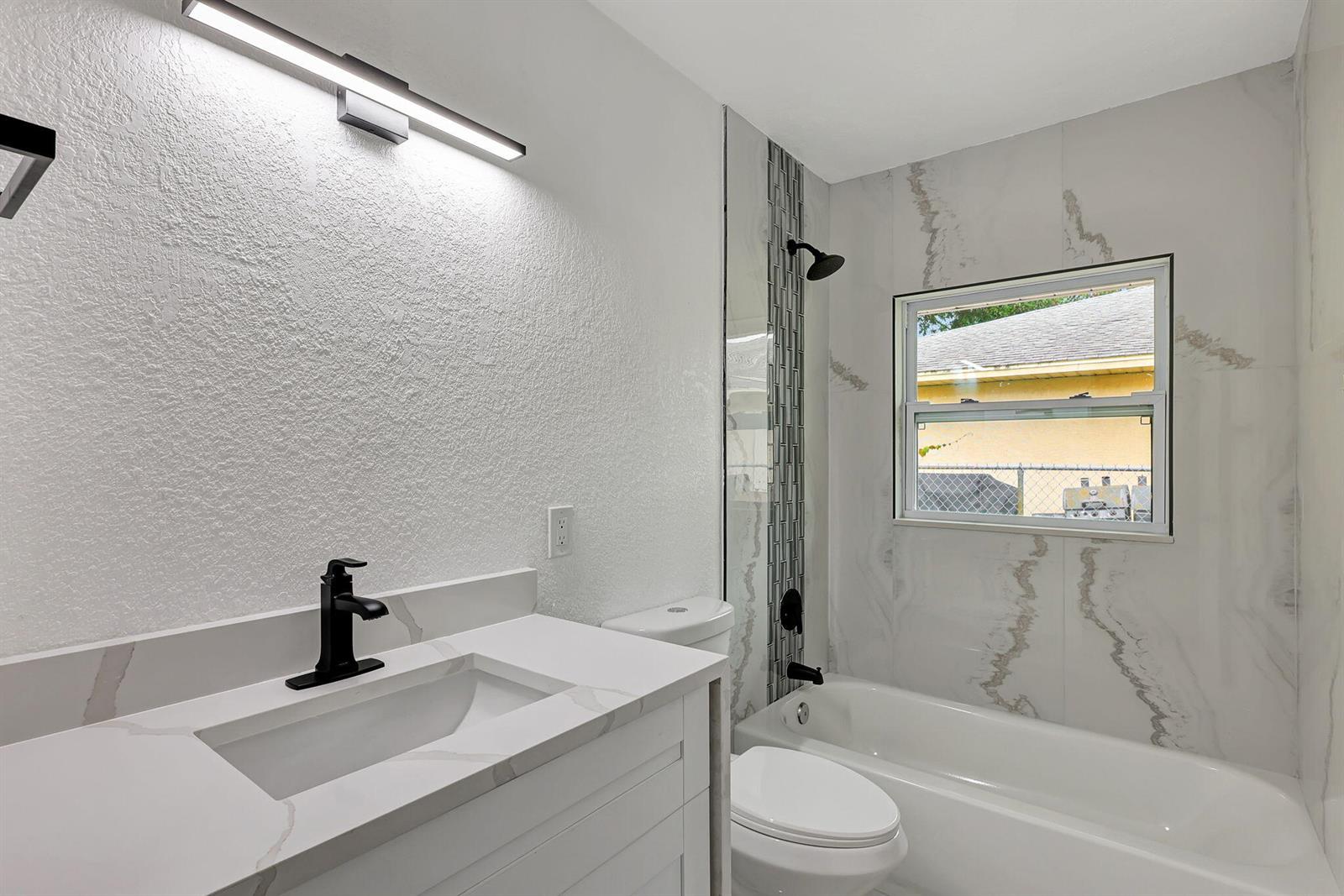 A bathroom features a white vanity, a toilet, and a shower-tub combo with marble-look tile — 1825 39th Avenue, Vero Beach FL 32960, VERO BEACH, FL