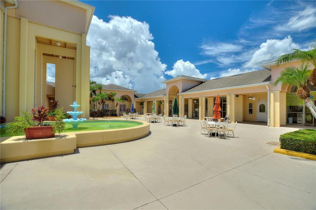 A courtyard features a tiered fountain, outdoor seating, and yellow buildings under a blue sky — 500 CLUB CIRCLE UNIT M, LAKESHORE, FL