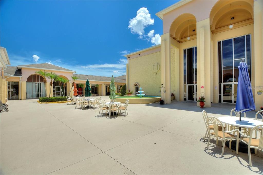 A paved outdoor courtyard features a central fountain, patio tables with umbrellas, and building facades — 500 CLUB CIRCLE UNIT M, LAKESHORE, FL