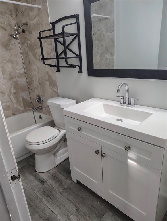 A kitchen features white cabinets, marble-look countertops, a tile backsplash, and gray wood-look flooring — 703 2ND AVENUE NW UNIT B, RUSKIN, FL