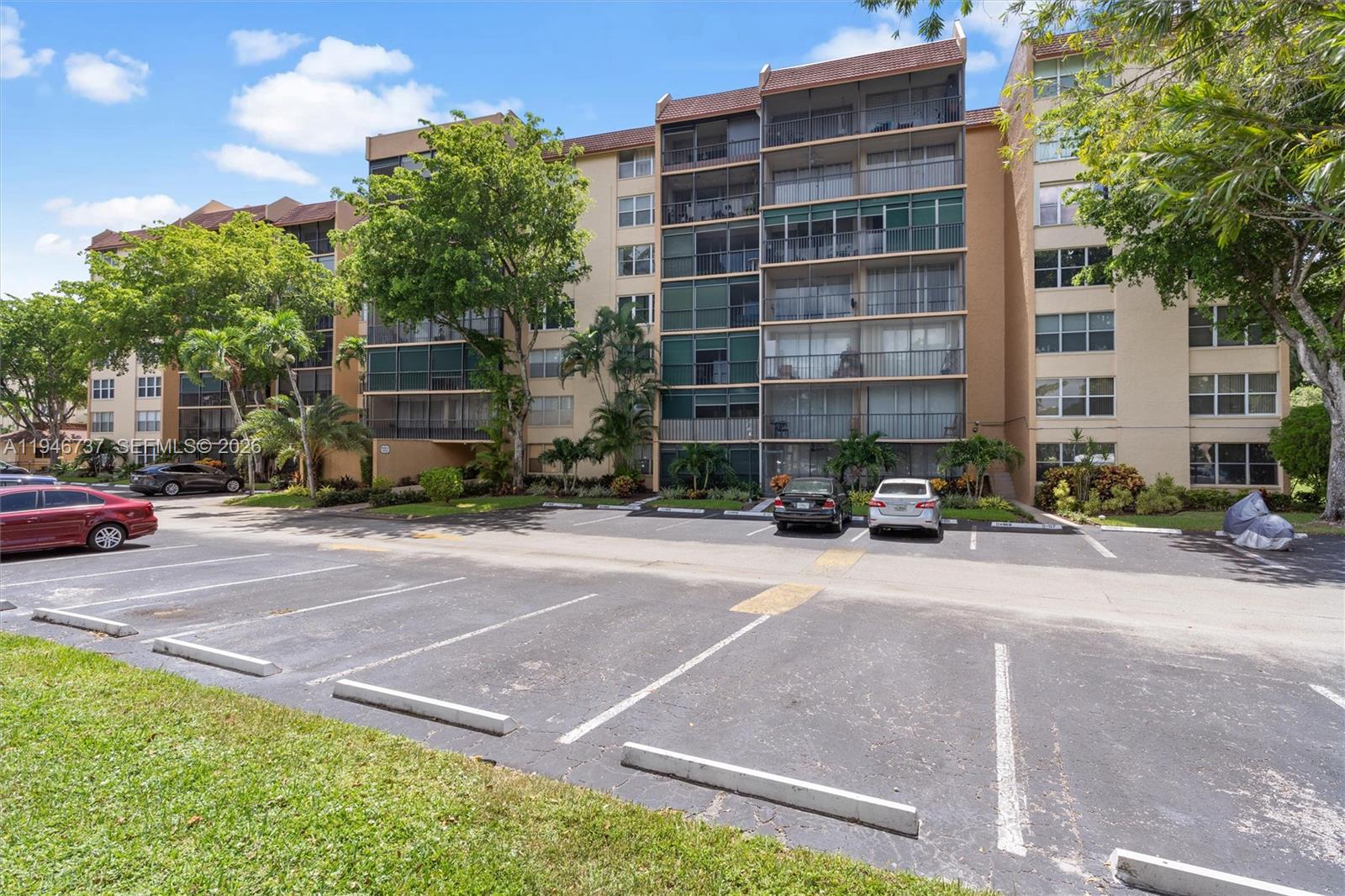 A multi-story apartment building stands behind a paved parking lot with several parked cars — 3771 Environ Blvd # 253, Lauderhill FL 33319, LAUDERHILL, FL