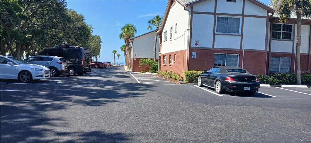A parking lot sits between two multi-story apartment buildings with palm trees and distant water — 650 PINELLAS POINT DRIVE S UNIT 110, ST PETERSBURG, FL