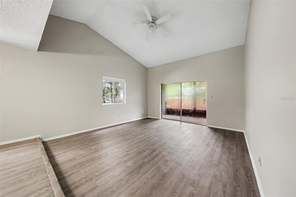 An empty room with vaulted ceilings, light wood-look flooring, a ceiling fan, and sliding doors — 871 BEACH BREEZE DRIVE, ORLANDO, FL