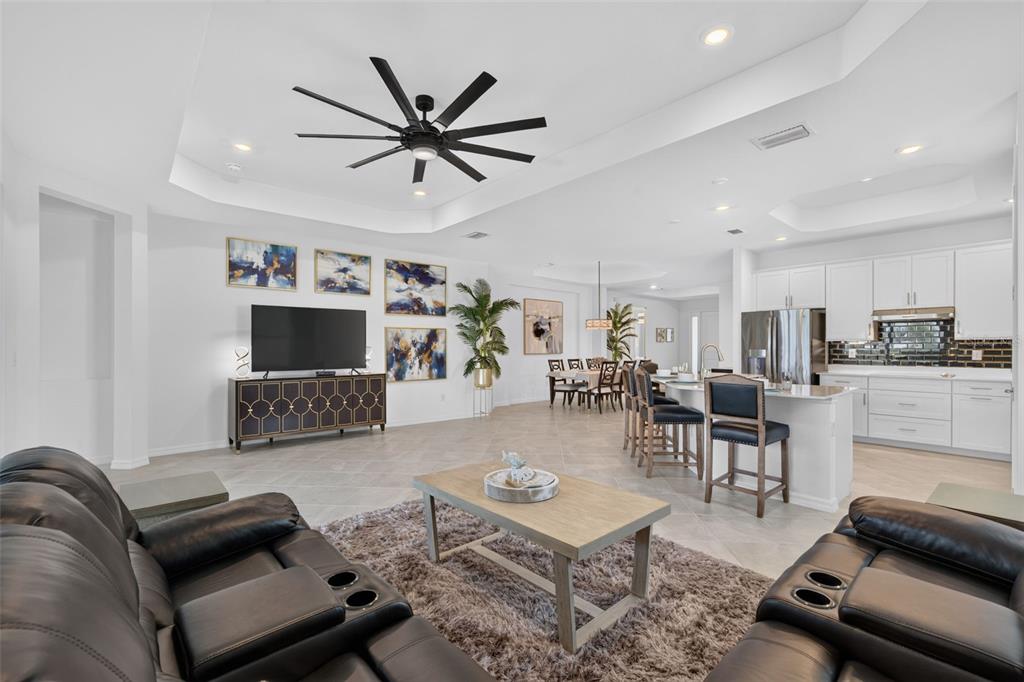 An open-concept living room and kitchen featuring a tray ceiling, tile floors, and dark furniture — 17260 JADESTONE COURT, VENICE, FL