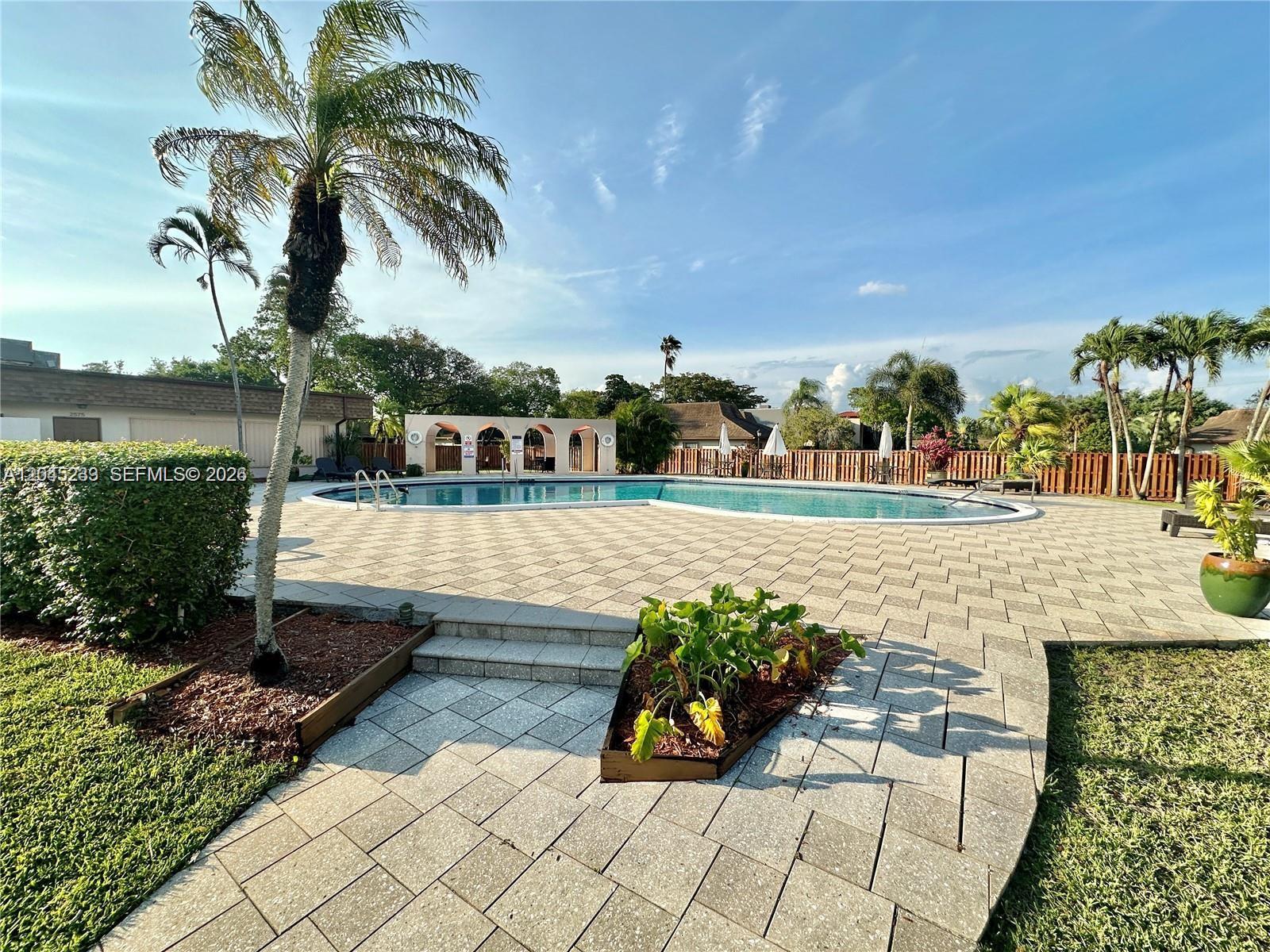 A paved patio surrounds a large outdoor swimming pool with a covered seating area — 7361 SW 26th Ct # 84, Davie FL 33314, DAVIE, FL