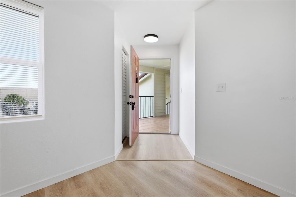 An entryway with light wood-look flooring leads to an open door revealing an outdoor balcony — 3038 PARKWAY BOULEVARD UNIT 306, KISSIMMEE, FL