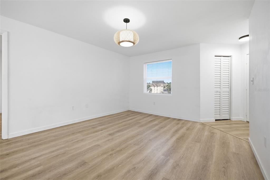 An empty room with white walls, light wood-look flooring, a window, and a hanging light fixture — 3038 PARKWAY BOULEVARD UNIT 306, KISSIMMEE, FL