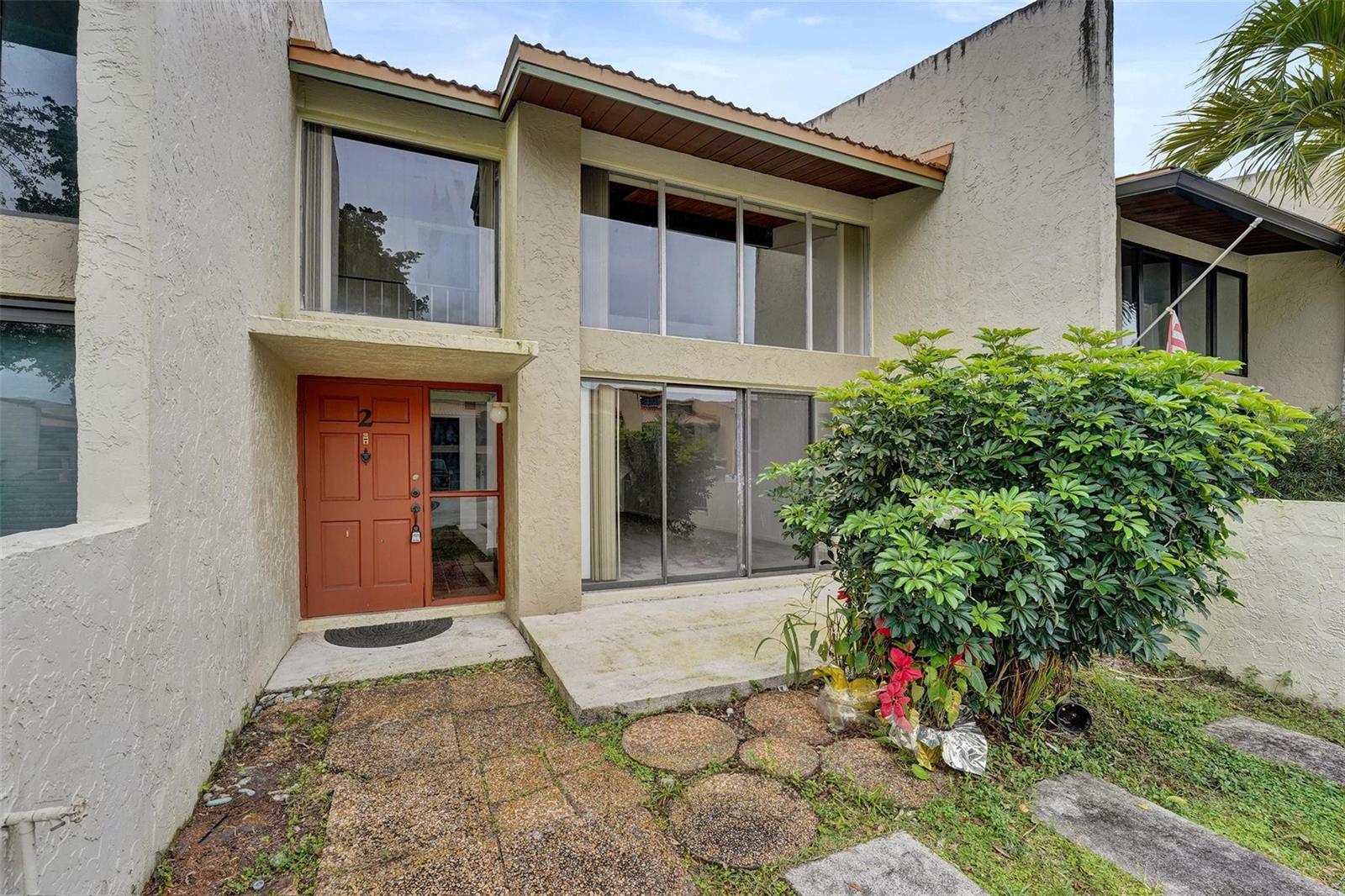 The exterior of a two-story townhouse features a red front door and large glass windows — 750 E Coco Plum Circle # 2, Plantation FL 33324, PLANTATION, FL
