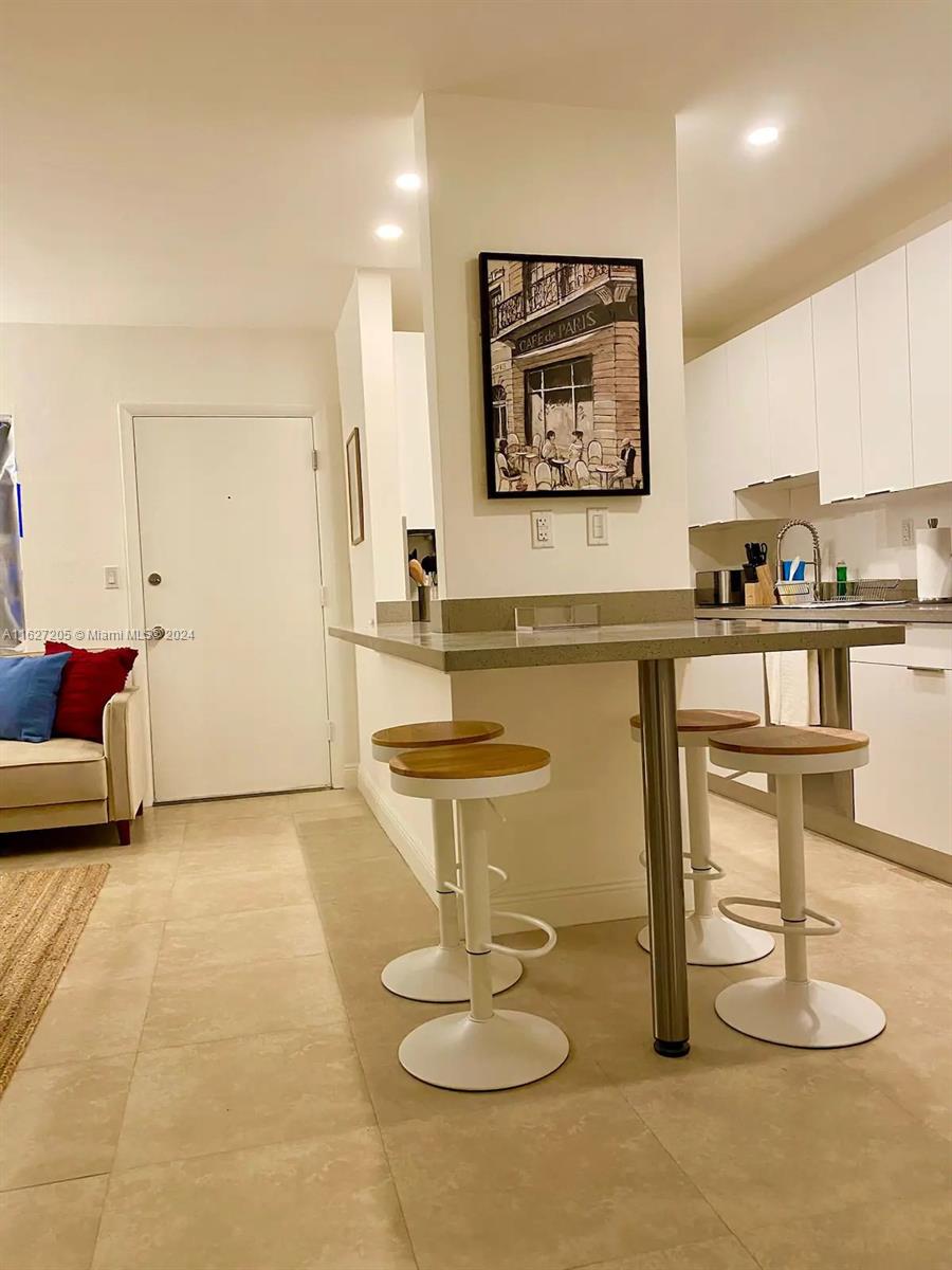 A kitchen with a breakfast bar and stools sits adjacent to a living area — 100 Sunrise Dr # 24, Key Biscayne FL 33149, KEY BISCAYNE, FL
