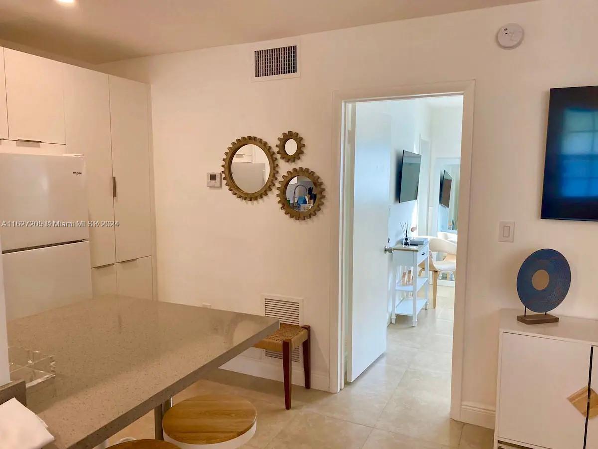 A kitchen with a stone island and white cabinets opens into a hallway with mirrors — 100 Sunrise Dr # 24, Key Biscayne FL 33149, KEY BISCAYNE, FL
