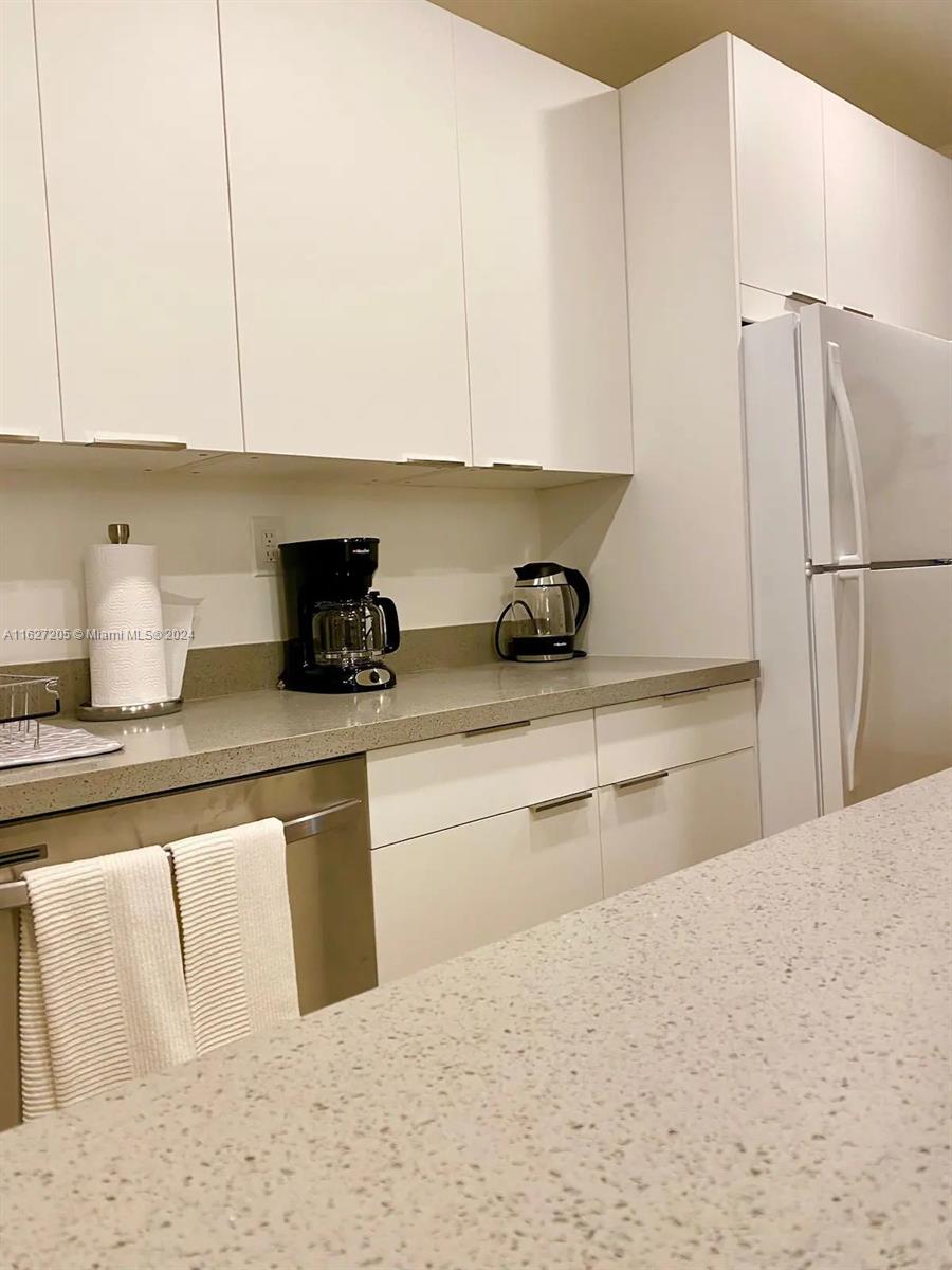 A kitchen features white cabinets, a stone countertop, and stainless steel appliances — 100 Sunrise Dr # 24, Key Biscayne FL 33149, KEY BISCAYNE, FL