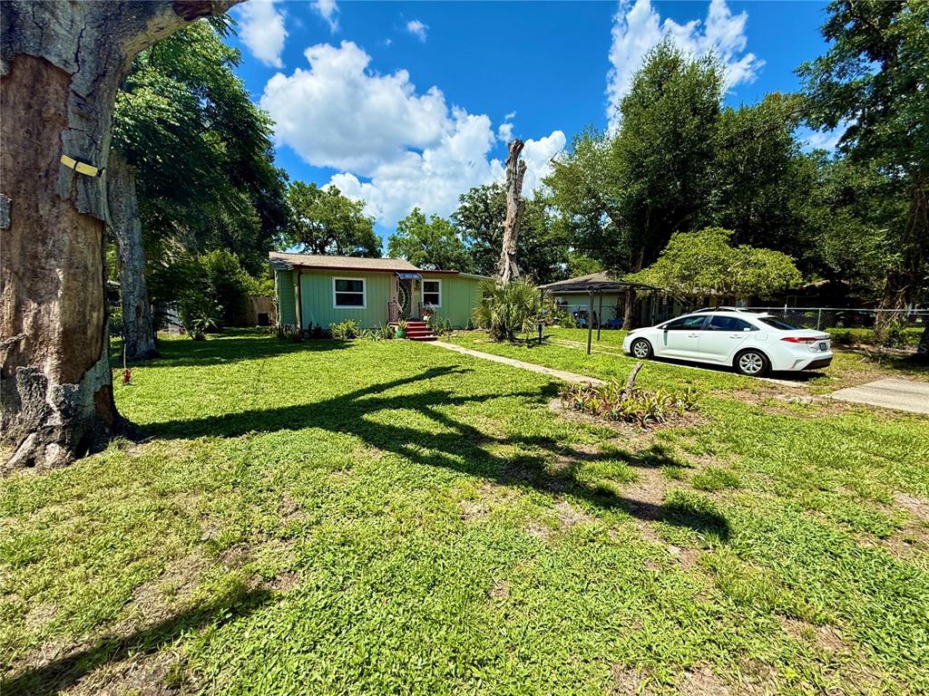 A light green house with a white car parked in the yard under large trees — 5937 UONA AVENUE, ORLANDO, FL
