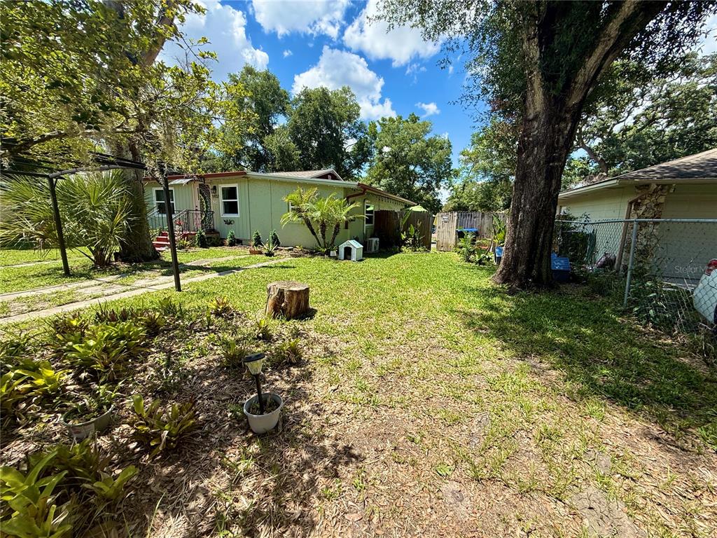 A grassy backyard features a light green house, mature trees, and a wooden fence — 5937 UONA AVENUE, ORLANDO, FL