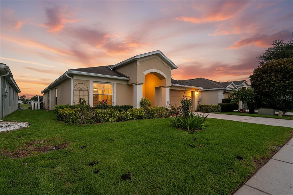 A single-story suburban house with a tan stucco exterior and arched entryway at sunset — 799 ALPINE THISTLE DRIVE, BROOKSVILLE, FL