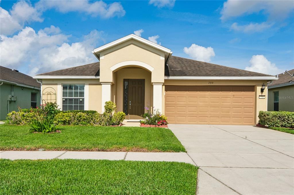 A single-story house with a tan stucco exterior, a brown garage door, and a front lawn — 799 ALPINE THISTLE DRIVE, BROOKSVILLE, FL