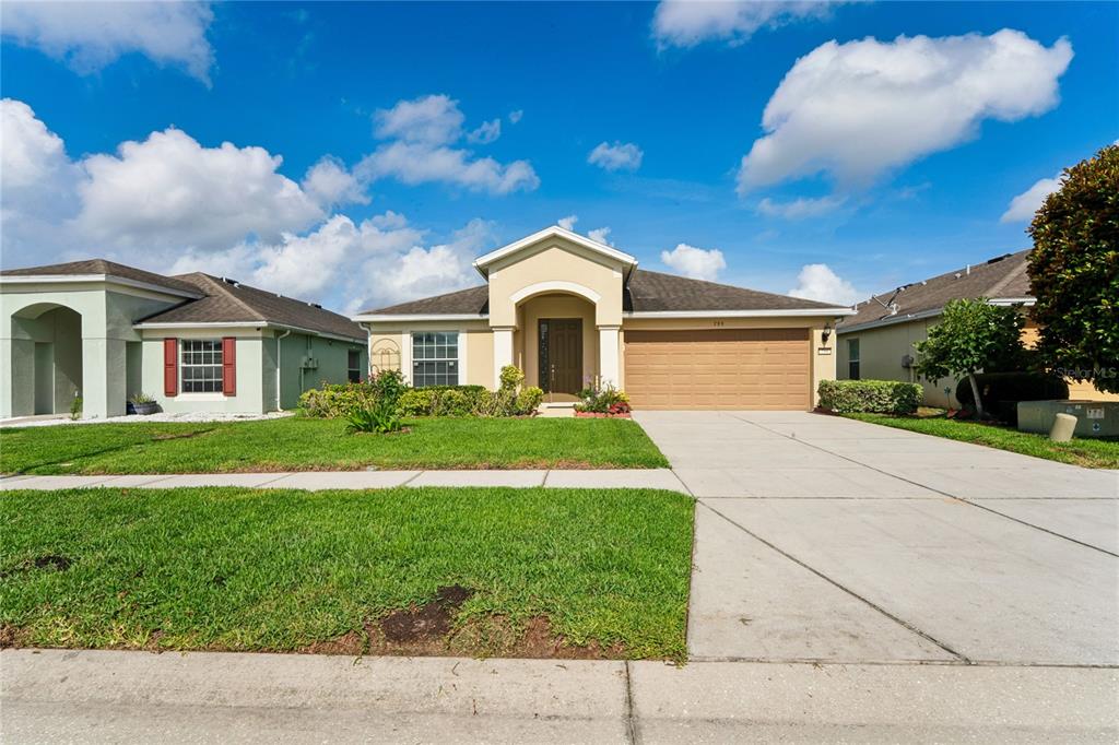 A single-story suburban house with a beige stucco exterior, a two-car garage, and a lawn — 799 ALPINE THISTLE DRIVE, BROOKSVILLE, FL