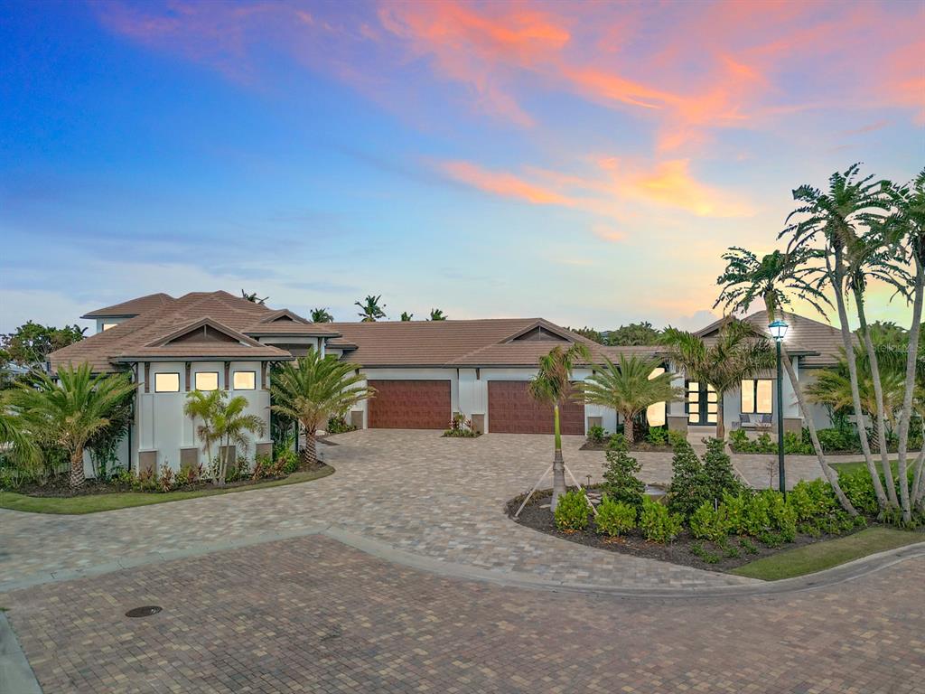 A large single-story house with a paved driveway, three-car garage, and palm trees at sunset — 14201 BAY DRIVE, FORT MYERS, FL
