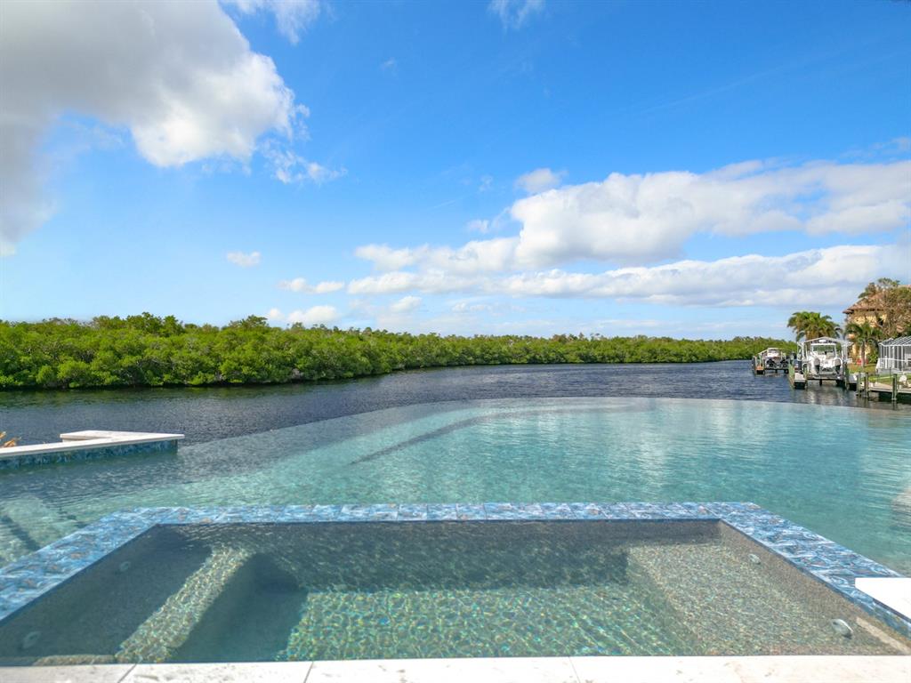 An infinity-edge pool and hot tub overlook a canal lined with mangroves and boats — 14201 BAY DRIVE, FORT MYERS, FL