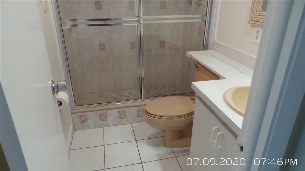 A bathroom features a beige toilet, a vanity with a sink, and a glass-enclosed shower — 2651 S Course Drive # 403, Pompano Beach FL 33069, POMPANO BEACH, FL