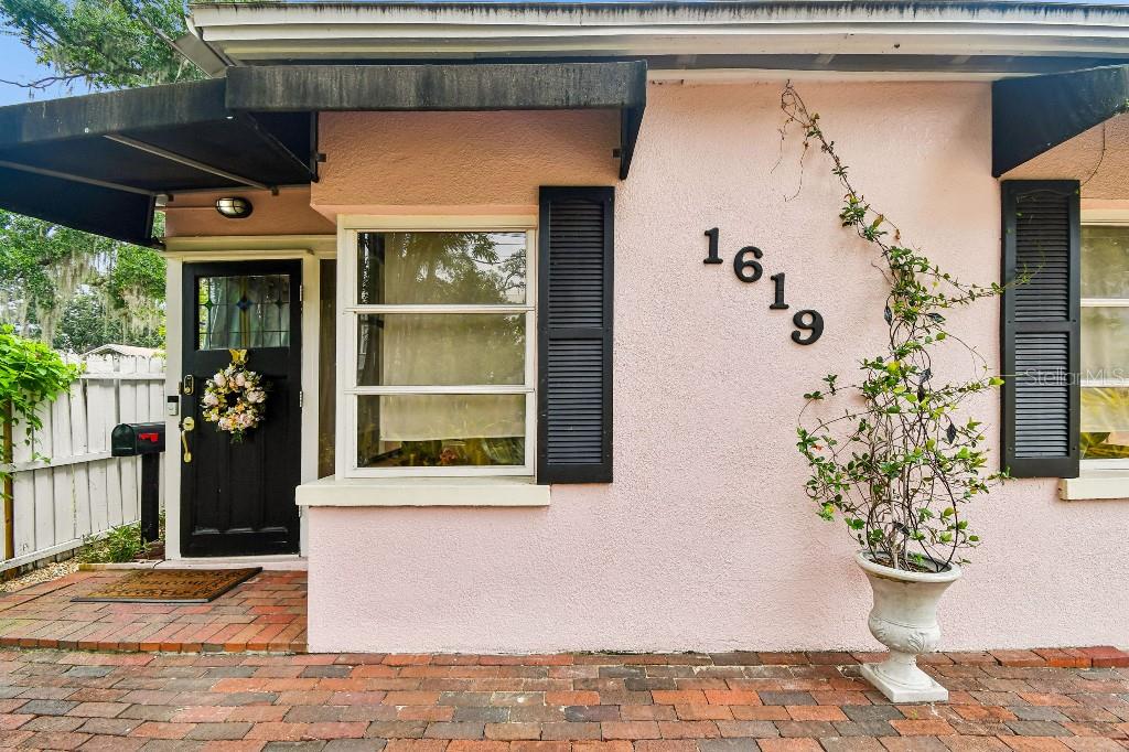A pink stucco house exterior features a black front door, shutters, and a brick patio — 1619 NEW YORK AVENUE, ORLANDO, FL