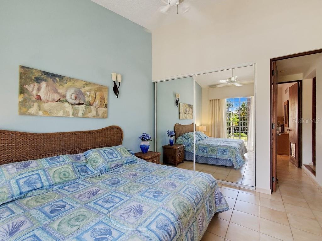 A bedroom features a wicker headboard, blue patterned bedding, mirrored closet doors, and tile flooring — 150 CANDELERO DRIVE UNIT 798, HUMACAO, PR