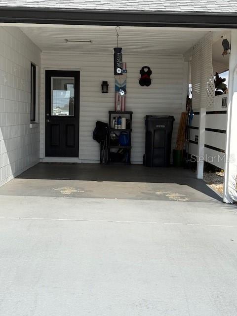 A covered carport area features a black door, a storage shelf, and a trash bin — 1021 AUGUSTA DRIVE, SUN CITY CENTER, FL