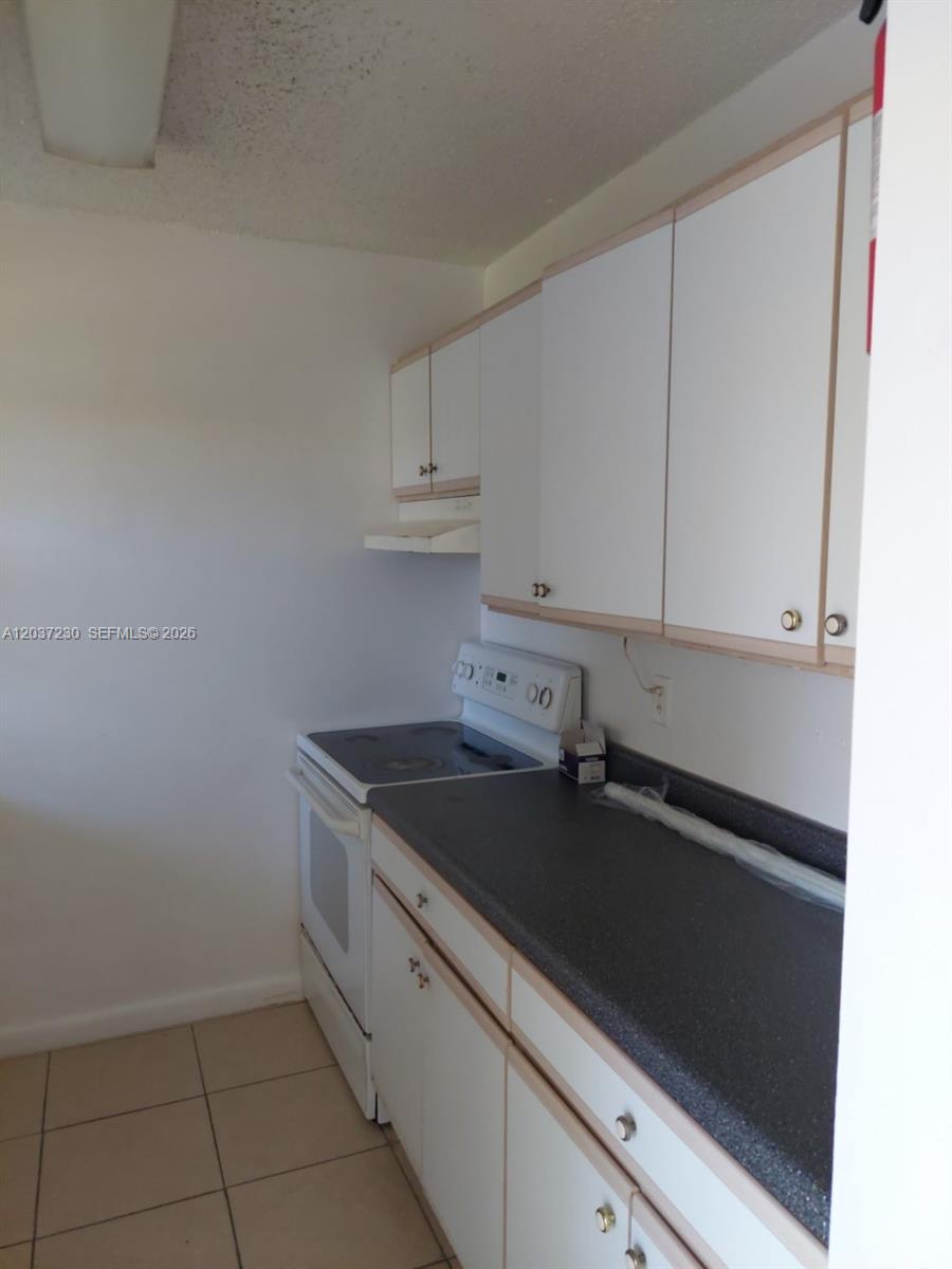 A galley-style kitchen features white cabinets, a dark countertop, and a white electric range — 2319 Johnson St # 1, Hollywood FL 33020, HOLLYWOOD, FL