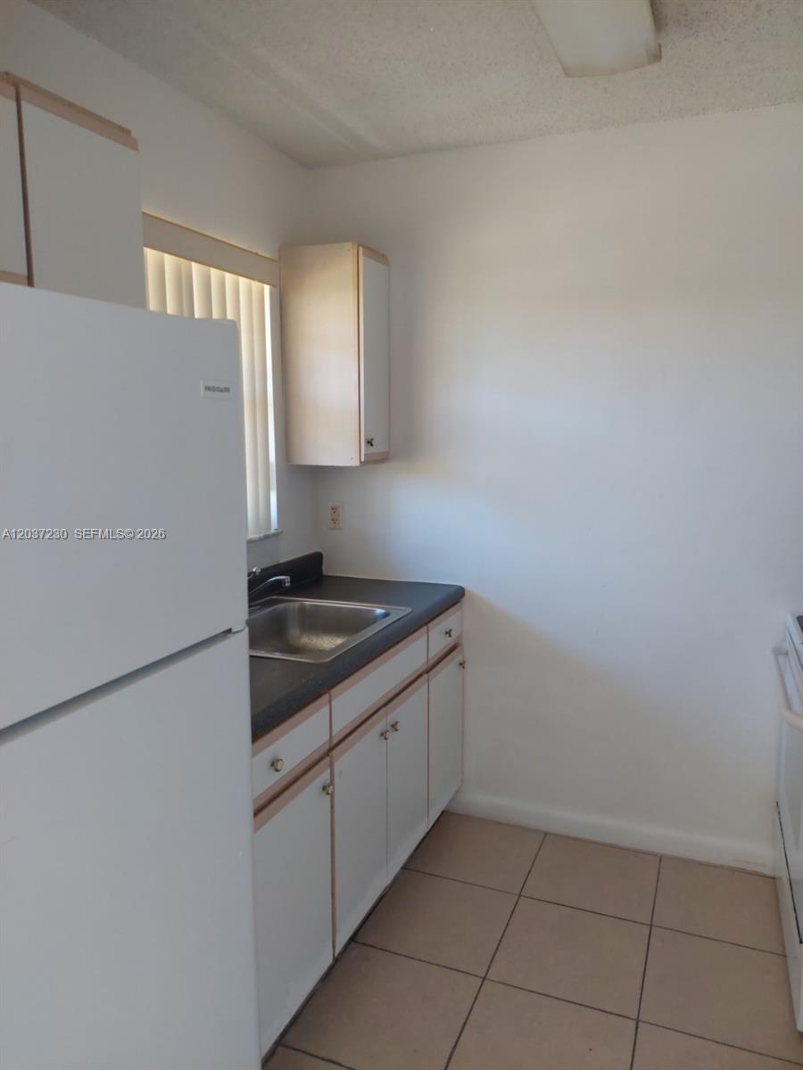 A small kitchen features white cabinets, a dark countertop, a sink, and a white refrigerator — 2319 Johnson St # 1, Hollywood FL 33020, HOLLYWOOD, FL