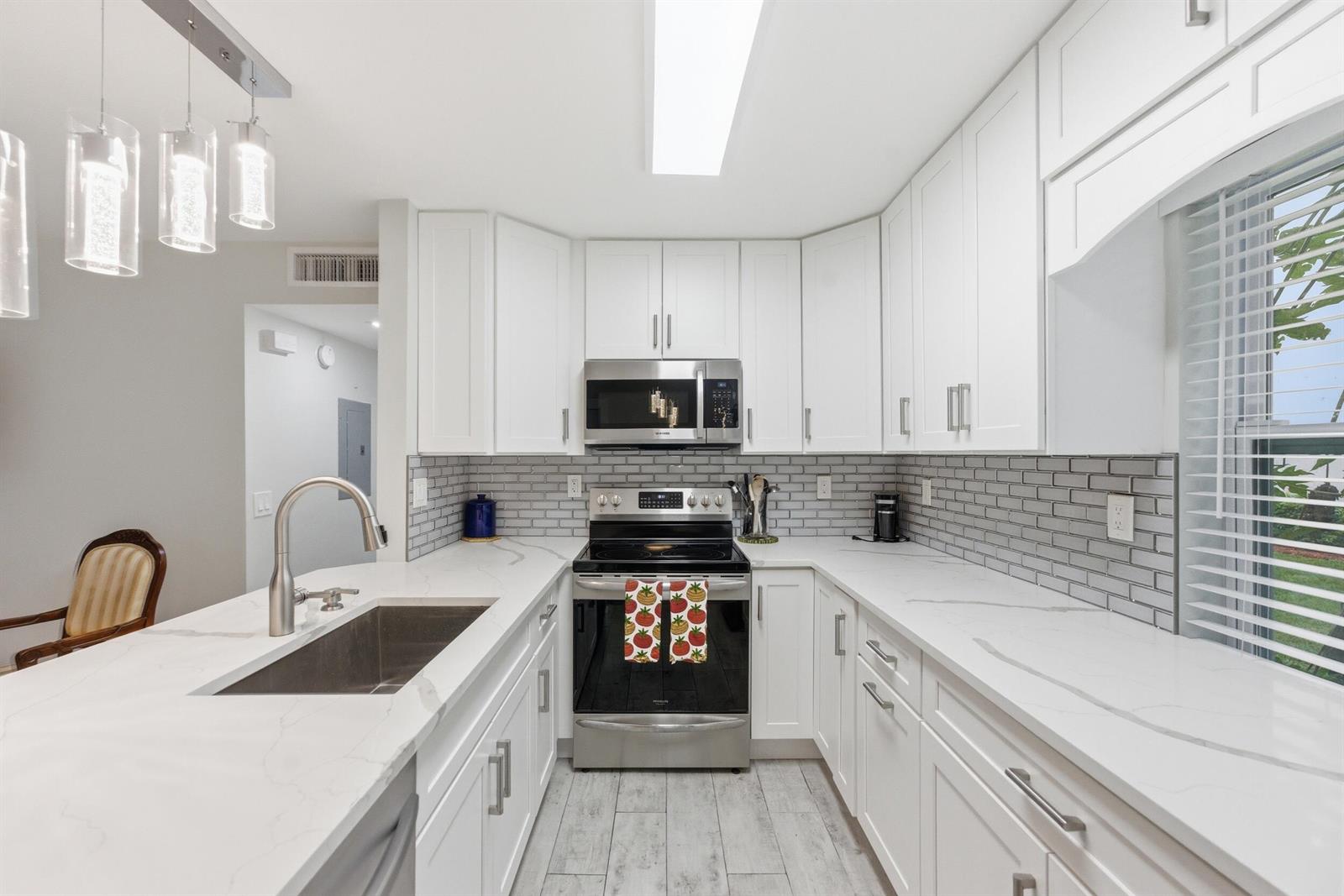A kitchen features white cabinets, marble-look countertops, stainless steel appliances, and a gray subway tile backsplash — 634 Normandy N, Delray Beach FL 33484, DELRAY BEACH, FL