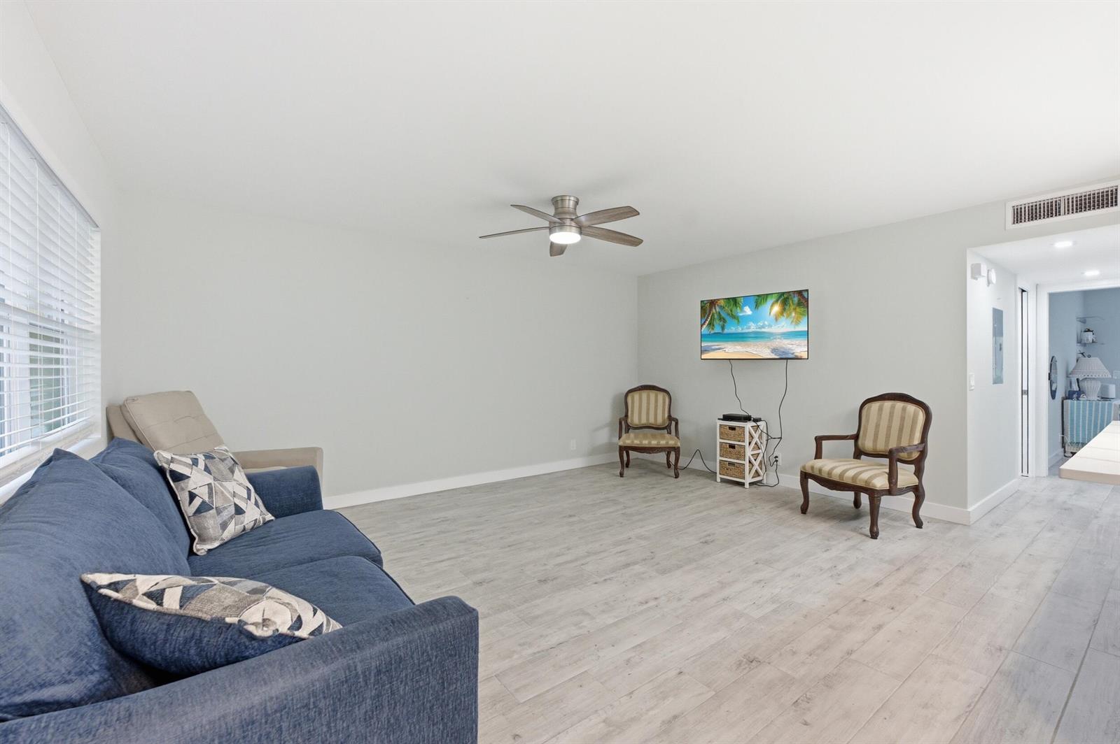A living room with light wood-look flooring, a blue sofa, and two patterned armchairs — 634 Normandy N, Delray Beach FL 33484, DELRAY BEACH, FL