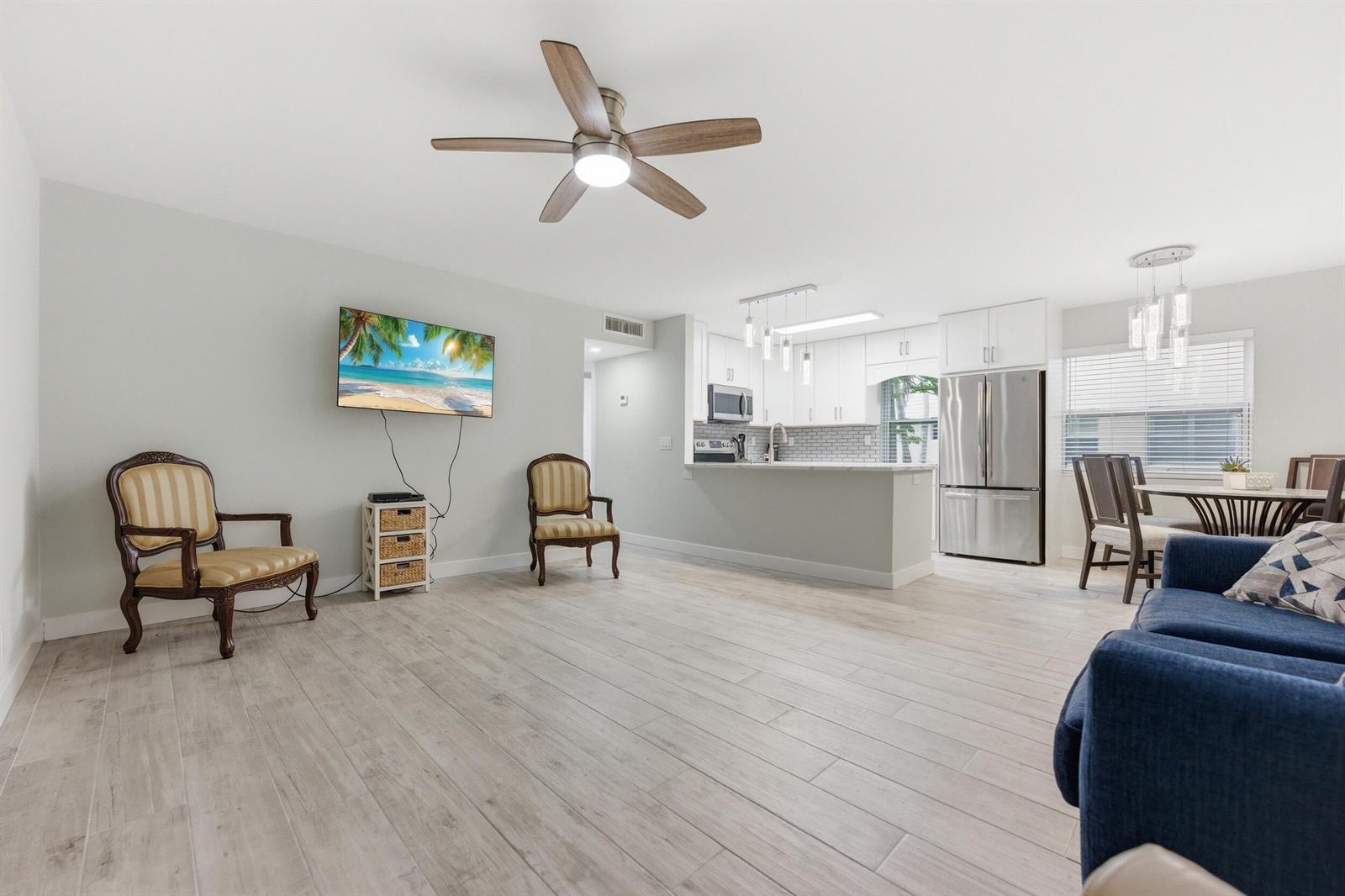 An open-concept living room and kitchen featuring light wood-look flooring and a ceiling fan — 634 Normandy N, Delray Beach FL 33484, DELRAY BEACH, FL