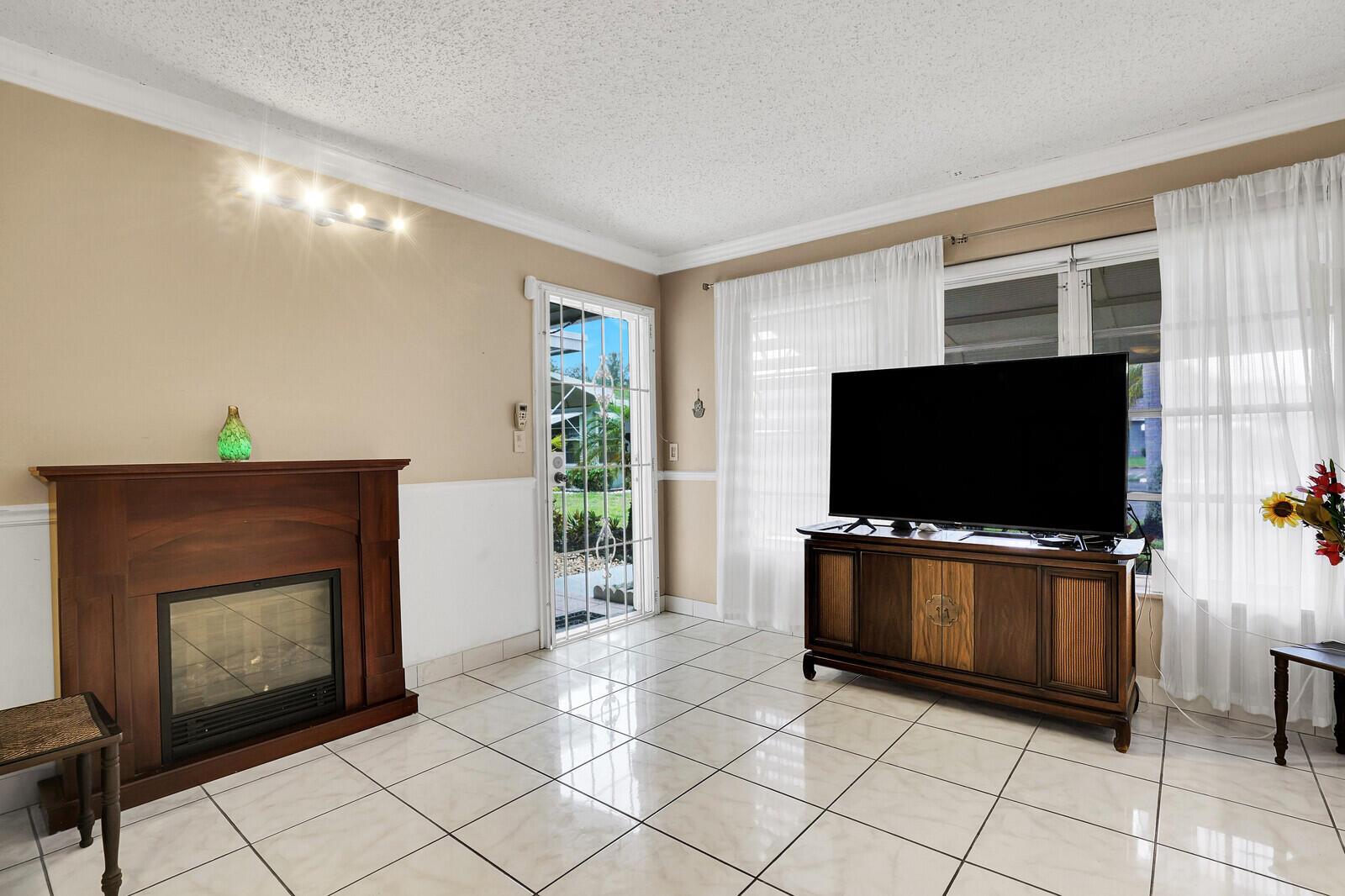 A living room features a fireplace, a television on a wooden console, and tile flooring — 902 South Drive # C, Delray Beach FL 33445, DELRAY BEACH, FL