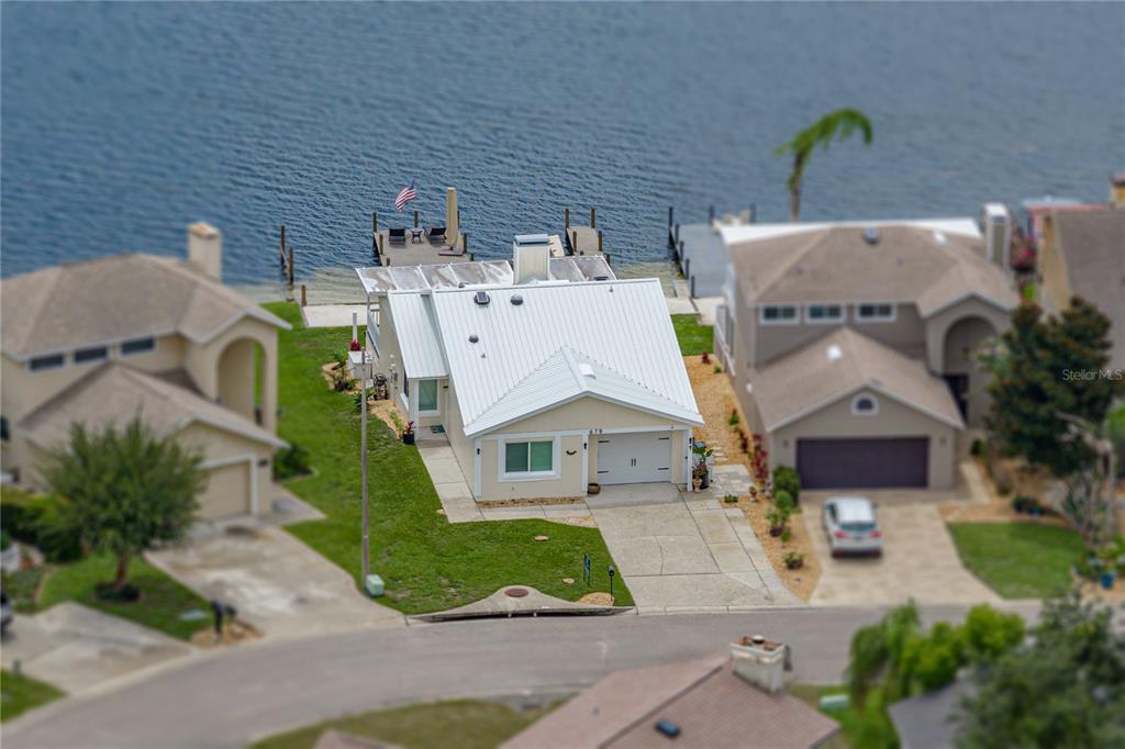 An aerial view shows a single-story house with a white metal roof and a dock — 679 LAKE DEXTER CIRCLE, WINTER HAVEN, FL