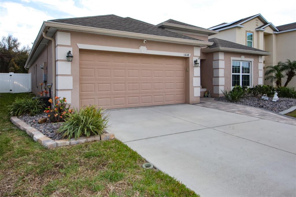 A single-story house with a beige stucco exterior, a two-car garage, and a paved driveway — 14148 FINSBURY DRIVE, SPRING HILL, FL