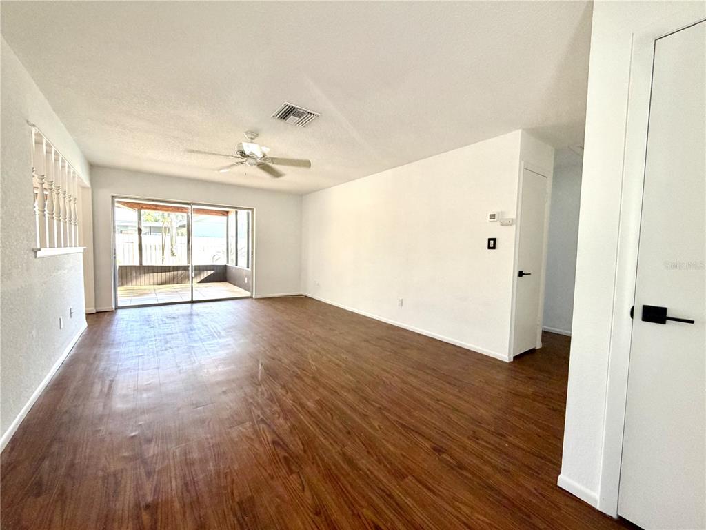 An empty living room features wood-look flooring, a ceiling fan, and a sliding glass door — 8212 101ST COURT, SEMINOLE, FL